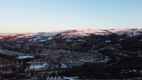 Drone-shot-of-the-winter-sun-glowing-on-the-snowy-hills-of-a-small-Yorkshire-town