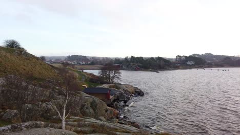 Panoramic-view-of-waves-hitting-small-cottage-on-rocky-cliff,-Sweden