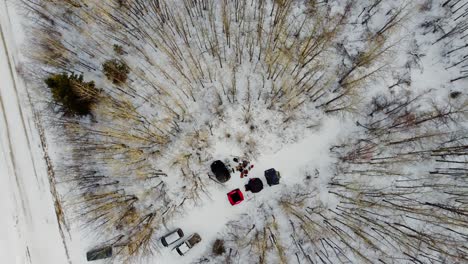 Aerial-Birds-Eye-View-Rise-over-winter-camping-with-tents-forming-a-V-with-a-campfire-dogs-entertained-on-a-sunset-with-bare-trees-tipped-in-golden-yellow-off-a-snow-covered-backroad-on-crown-land-3-3