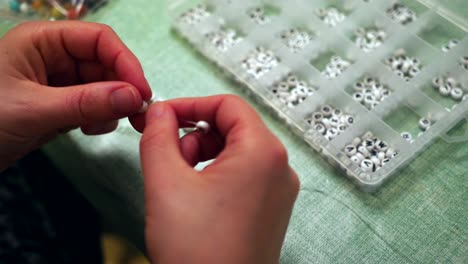 Person-stringing-through-white-beads-with-letters-to-make-a-bracelet,-close-up