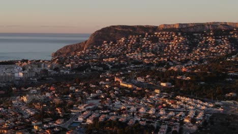 Drone-footage-over-the-town-of-Calpe,-with-the-Mediterranean-sea-in-the-background,-on-a-bright-sunlit-morning,-at-sunrise