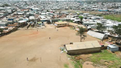 Poor-school-children-moving-out-of-school,-poor-African-ethnical-people-passing-over-the-brown-field,-poor-sheet-Settlement-surrounding-the-football-pitch-in-kibera-Nairobi-kenya