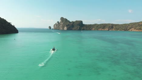 Long-Tail-Boat-sailing-through-idyllic-emerald-green-sea-in-Loh-Dalum-Bay-in-Ko-Phi-Phi-Don-Island,-Thailand---Aerial-Fly-over-panorama-shot