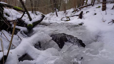 creek-flowing-under-ice-in-a-wood-covered-with-snow-in-winter,-jib-up