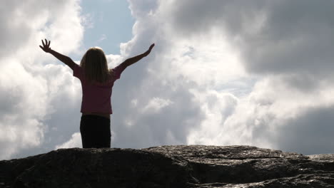 Back-view-of-child-girl-standing-on-rock-and-raising-arms-to-the-sky