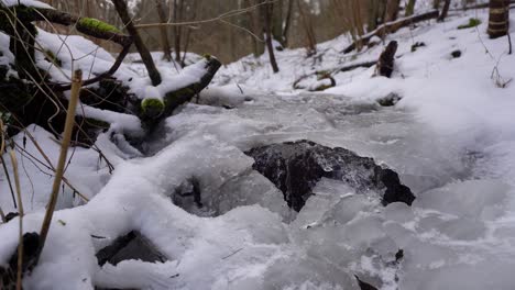 creek-flowing-under-ice-in-a-wood-covered-with-snow-in-winter,-slow-jib-up