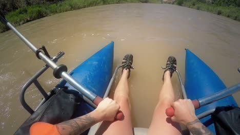 POV-shot-of-tattooed-woman-rowing-an-inflatable-pontoon-boat-in-a-muddy-river-in-Black-Rocks-Canyon,-Colorado