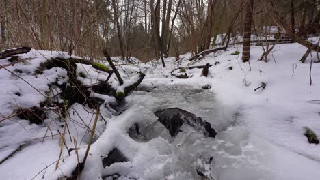 creek-flowing-under-ice-in-a-wood-covered-with-snow-in-winter,-jib-down