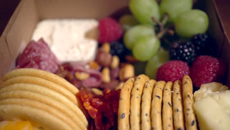 A-charcutterie-snack-box-with-cooked,-cured-meats,-crackers,-grapes,-berries-and-cheese---rotating-focus-pull