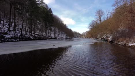 calm-river-with-remaining-ice-and-snow-in-the-woods,-day,-winter,-jib-up