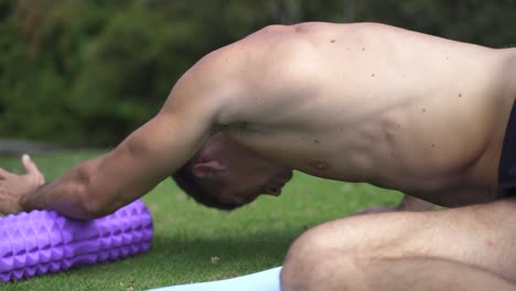 Young-caucasian-fit-attractive-male-exersicing-outdoors-Foam-roller-dorsal-exercise-with-green-vegetation-background-slow-motion-60-fps