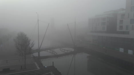 Jib-up-of-cyclist-bicycling-over-small-bridge-over-river-in-fogged-covered-Dutch-city
