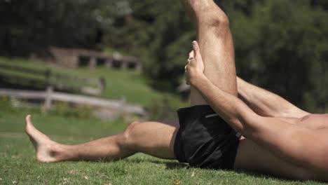 4K-Young-caucasian-fit-attractive-male-exersicing-outdoors-with-green-vegetation-background-hamstrings-mobility-exercise