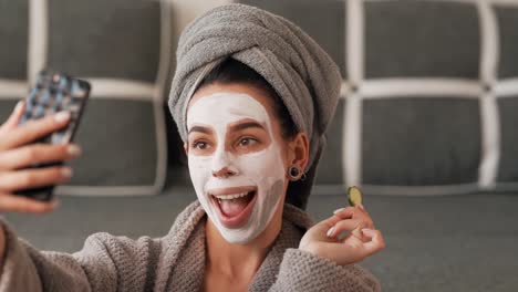Beautiful-girl-in-a-gray-towel-robe-makes-a-selfie-face-in-a-clay-mask