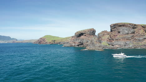 Luxury-boat-exploring-wild-shore-of-remote-Ilhéu-do-Farol-on-sunny-day