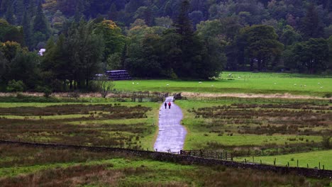 Two-distant-walkers-follow-a-path-back-to-Patterdale-in-the-Lake-District-on-a-rainy-day,-near-Ullswater,-Cumbria,-England,-UK