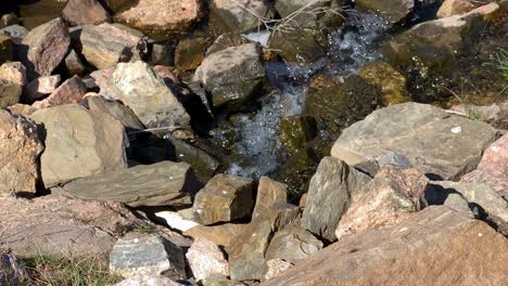 Wasser,-Das-An-Einem-Sonnigen-Tag-Zwischen-Felsen-In-Einem-Winzigen-Gebirgsbach-Fließt