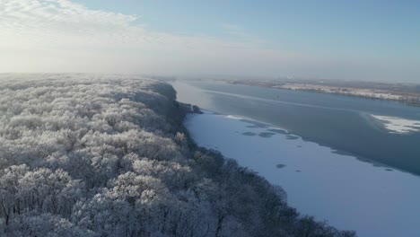 Flying-low-over-frosty-treetops-revealing-coastal-road-and-wast-icy-river