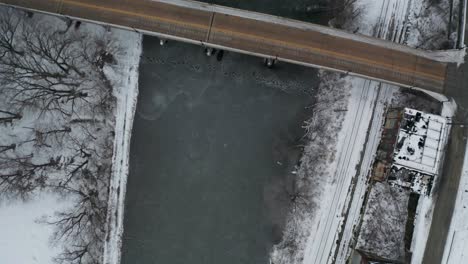 Top-down-aerial-view-of-frozen-river-and-small-road-bridge-in-urban-area
