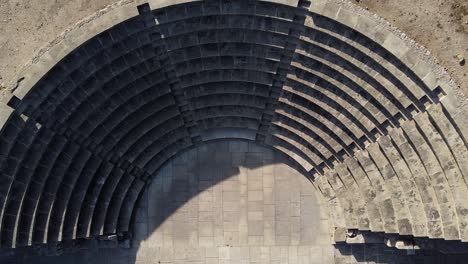 An-ancient-Greek-Odeon,-sinking-top-down-aerial-view-zooming-in-close-on-the-stone-seating