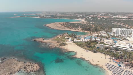 Clear-shallow-Turquoise-waters-complementing-pristine-Nissi-Beach-Coast,-in-Ayia-Napa,-Cyprus---Aerial-high-slow-panoramic-shot