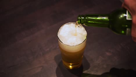 Die-Hand-Des-Mannes-Gießt-Ein-Bier-Aus-Der-Grünen-Flasche-In-Ein-Glas,-Nahaufnahme-Von-Oben