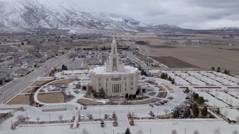 Aerial-orbit-shot-of-beautiful-architecture-named,-Payson-Utah-Temple,-LDS-Mormon-Church-with-dramatic-snow-covered-mountain-landscape-and-grey-clouds