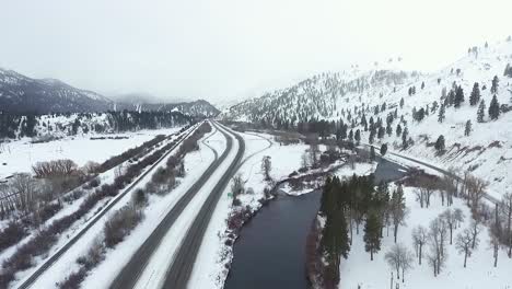 AERIAL---rural-highway-follows-cold-river-during-snowstorm