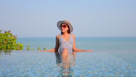 Close-up-of-a-young-attractive-woman-lounging-in-a-resort-pool-against-an-ocean-background
