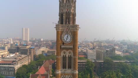 Drone-shot-of-the-Rajabai-Clock-Tower-next-to-the-Bombay-High-Court-Building-and-Oval-Maidan,-an-ornate-1878-clock-tower-modeled-after-Big-Ben-and-featuring-stained-glass-windows-and-musical-chimes