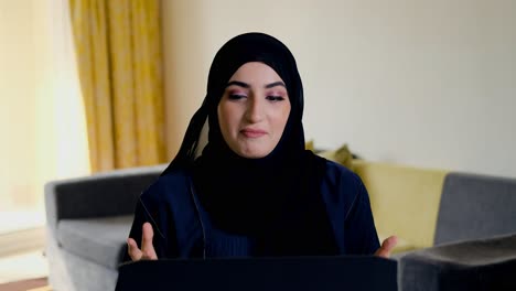 Glückliche-Arabische-Frau-Bei-Online-Videokonferenzanrufen-Mit-Laptop,-Die-Aus-Der-Ferne-Arbeitet-Und-Kulturelle-Haarbedeckungen-Aus-Dem-Nahen-Osten-Trägt,-Die-Abaya-Und-Hijab-Genannt-Werden