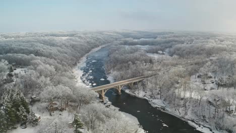 Blick-Aus-Der-Vogelperspektive-Auf-Die-Majestätische-Brücke-über-Den-Zugefrorenen-Fluss-Und-Den-Frostigen-Wald