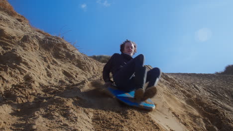 Happy-boy-slides-down-sand-dune-on-a-sledge