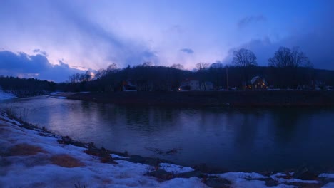 Nightfall-timelapse-in-late-winter-in-small-town-America,-over-a-river-with-some-snow-still-on-the-ground-and-colorful-skies-and-clouds-in-New-York-State-in-Rosendale,-Ulster-County,-Hudson-Valley