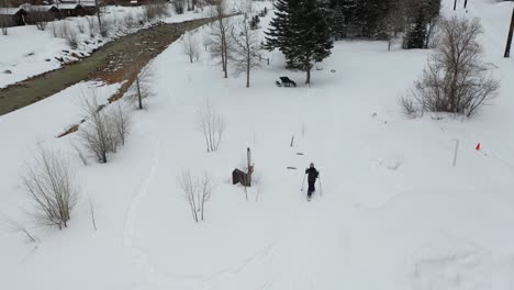 Aerial-view-of-lonely-woman-in-snowshoes-walking-on-snow-at-winter-hiking-trail-by-the-river-near-Ouray,-southwestern-Colorado-USA,-tilt-up-drone-shot