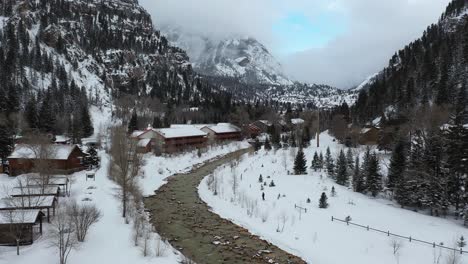 Aerial-view-of-lonely-person-walking-on-snow-by-the-river-in-winter-landscape-of-scenic-Ouray-valley,-southwestern-Colorado-USA,-drone-shot-on-light-snowfall