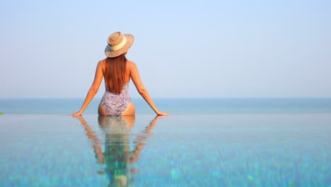 Rear-View-of-Woman-Sitting-by-the-Pool,-Body-Reflecting-in-Water-SLOMO