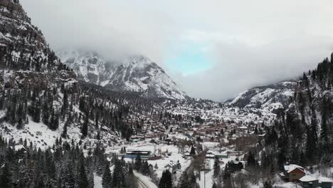 Aerial-view-of-Ouray,-Colorado-in-snowy-winter-landscape,-Switzerland-or-America-under-steep-hills-of-San-Juan-mountains,-drone-shot