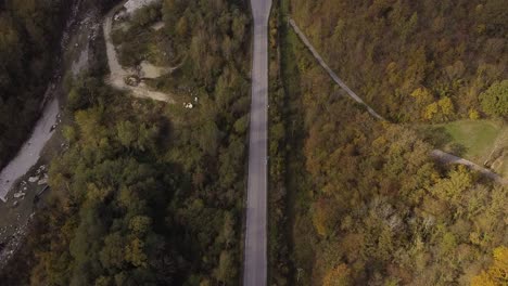 Aerial-view-of-a-riverside-country-road-through-the-Apennine-mountains-forest,-Italy