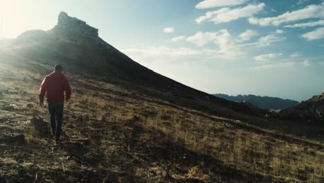 Rear-view-of-man-in-red-jacket-walking-towards-mountain-in-Lebanon,-sunset,-tracking-shot