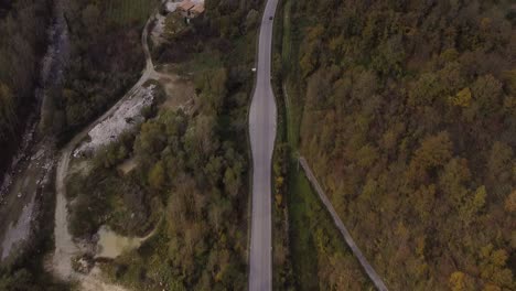 Aerial-landscape-view-of-a-riverside-country-road-through-the-Apennine-mountains-forest,-Italy