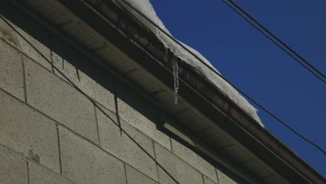 Icicle-Dripping-On-Gutter-Of-A-House-Roof-Against-Blue-Sky
