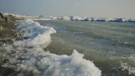 Wasser,-Das-Auf-Eis-Spritzt,-Bildete-Sich-An-Einem-Eiskalten-Ufer-Während-Eines-Sonnigen-Wintertages