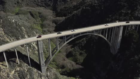 Aerial-pan-down,-Bixby-Canyon-Bridge,-cars-on-road,-Big-Sur-coast,-California