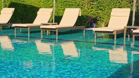 Empty-Lounge-Chairs-near-Sunny,-Blue-Hotel-Swimming-Pool