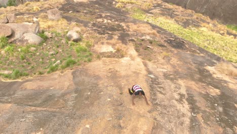 Aerial-shot-looking-down-a-granite-cliff-as-a-young-African-man-climbs-up-the-sheer-face
