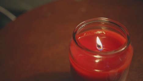 Burning-Candle-On-A-Glass-Jar-Placed-On-A-Wooden-Table---close-up