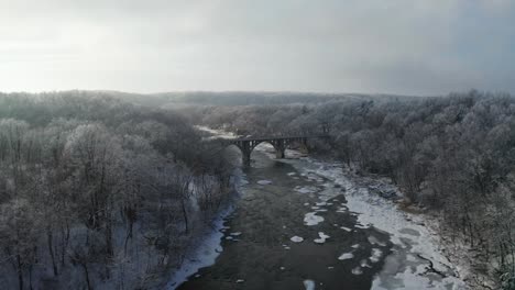 Annäherung-An-Die-Majestätische-Brücke-über-Den-Zugefrorenen-Winterfluss,-Umgeben-Von-Frostigem-Weißem-Wald
