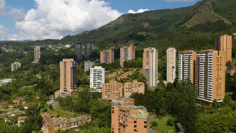 Drone-Descends-in-Poblado,-Medellin,-Colombia-with-Beautiful-Landscape-of-Andes-Mountains-in-Background