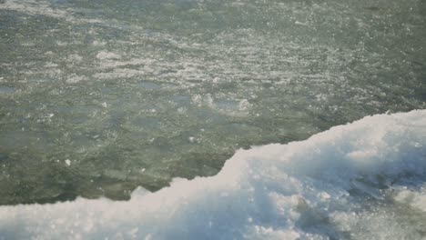Weißer-Frischer-Schnee-Am-Ufer-Mit-Eisigem-Kristall,-Der-Auf-Der-Oberfläche-Schwimmt